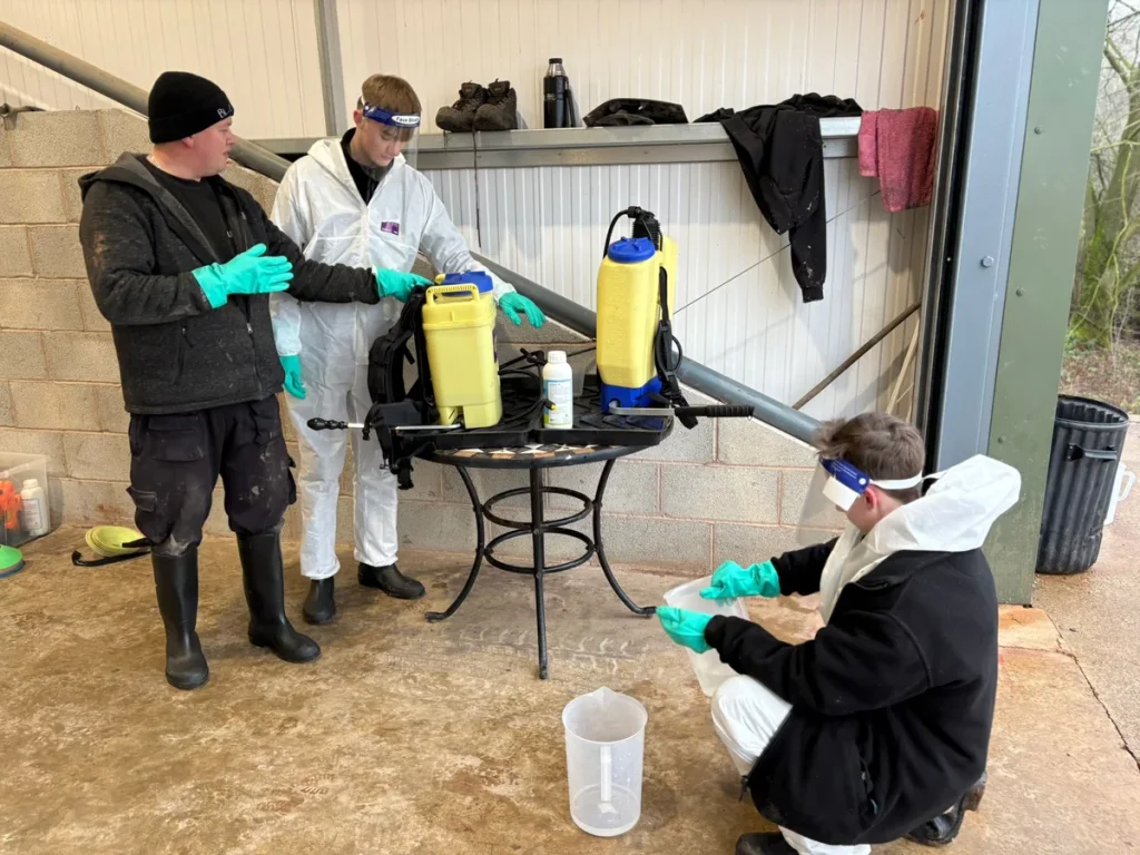 Trainees in protective suits learning to use knapsack sprayers